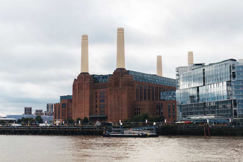 This image depicts a view of a large industrial building with three tall, white smokestacks against a vibrant pink and purple sunset sky. The building is made of red brick and features architectural d